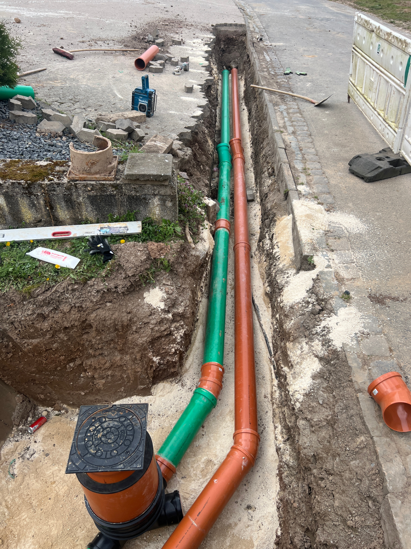 Offene Baugrube mit neu verlegten Kanalrohren in Grün und Orange entlang einer Straße